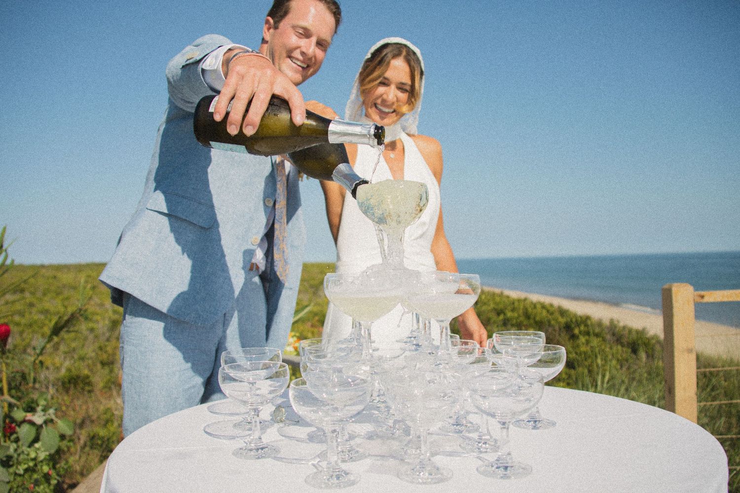 Creating champagne tower at beachside wedding reception with ocean backdrop.