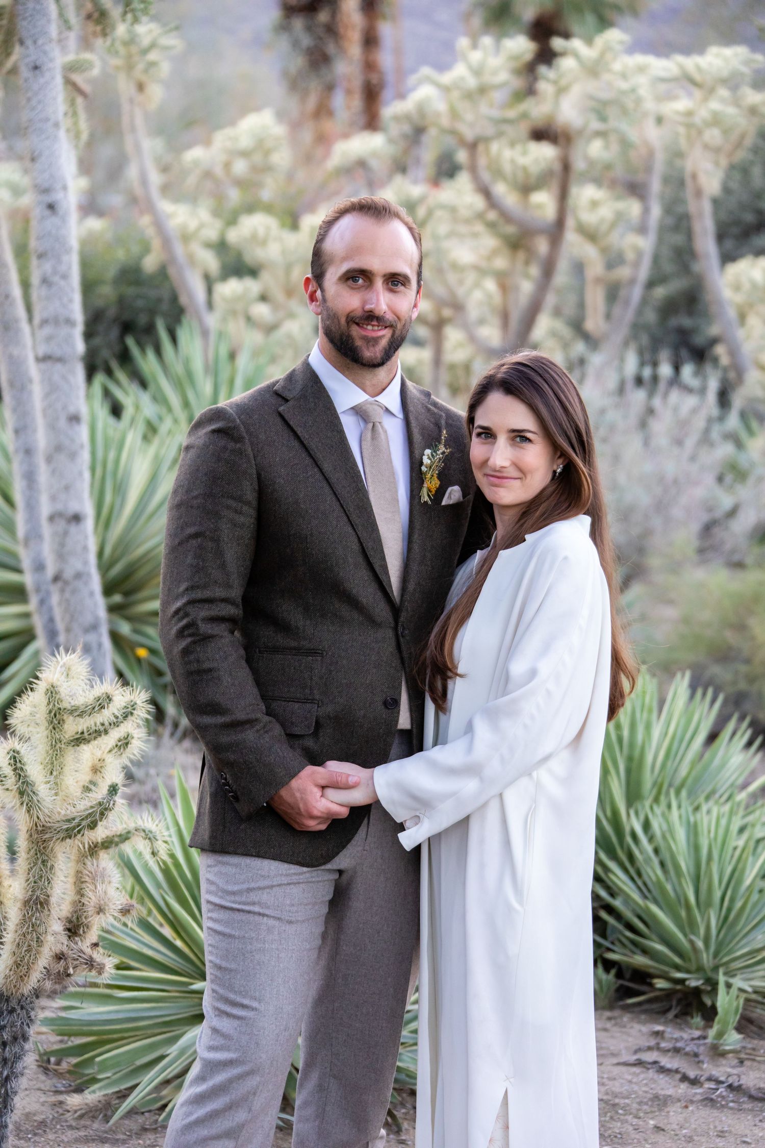 Wedding couple embraces among desert plants and palm trees.