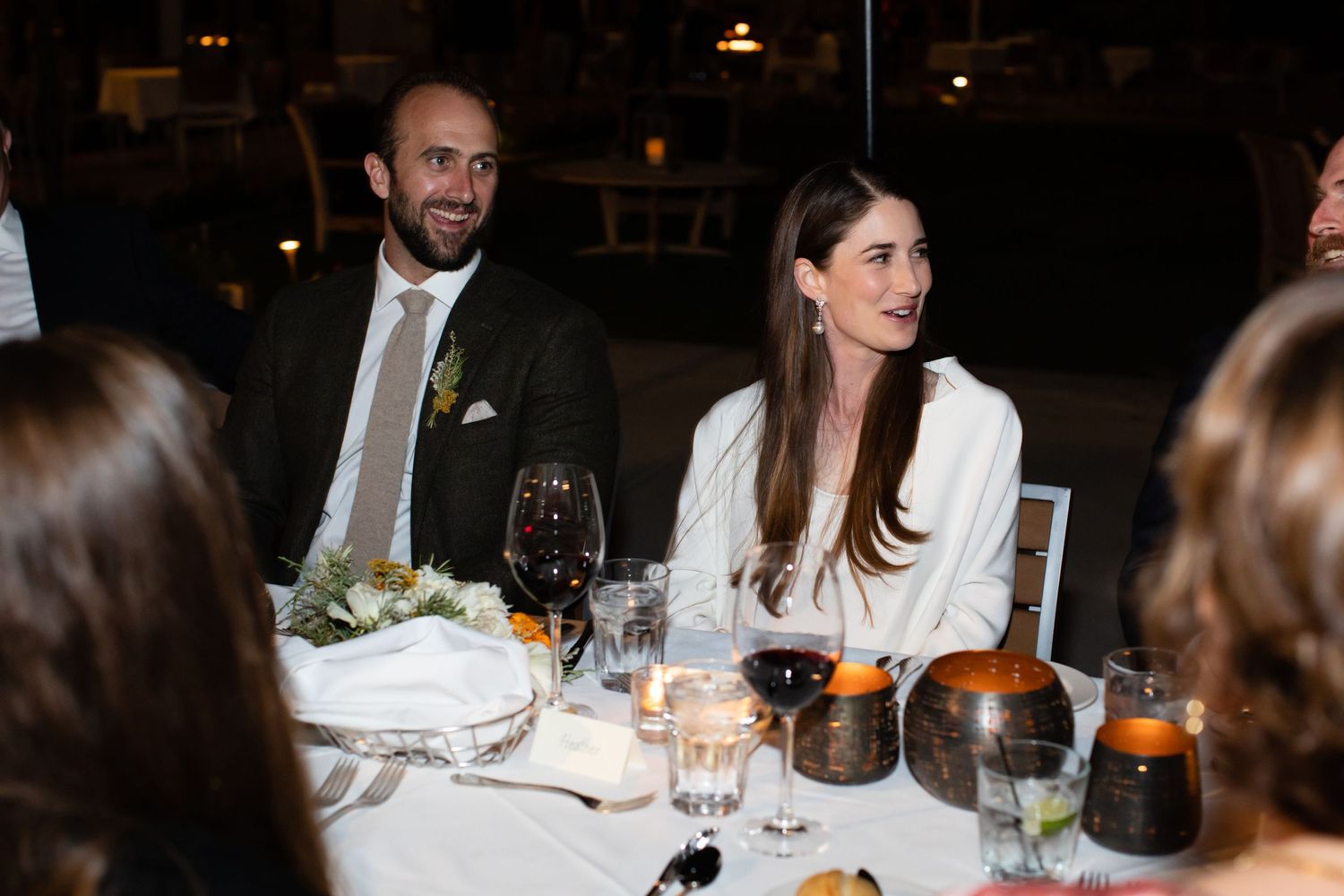 Wedding guests enjoying dinner and conversation at an elegant indoor reception with stone walls and warm lighting.