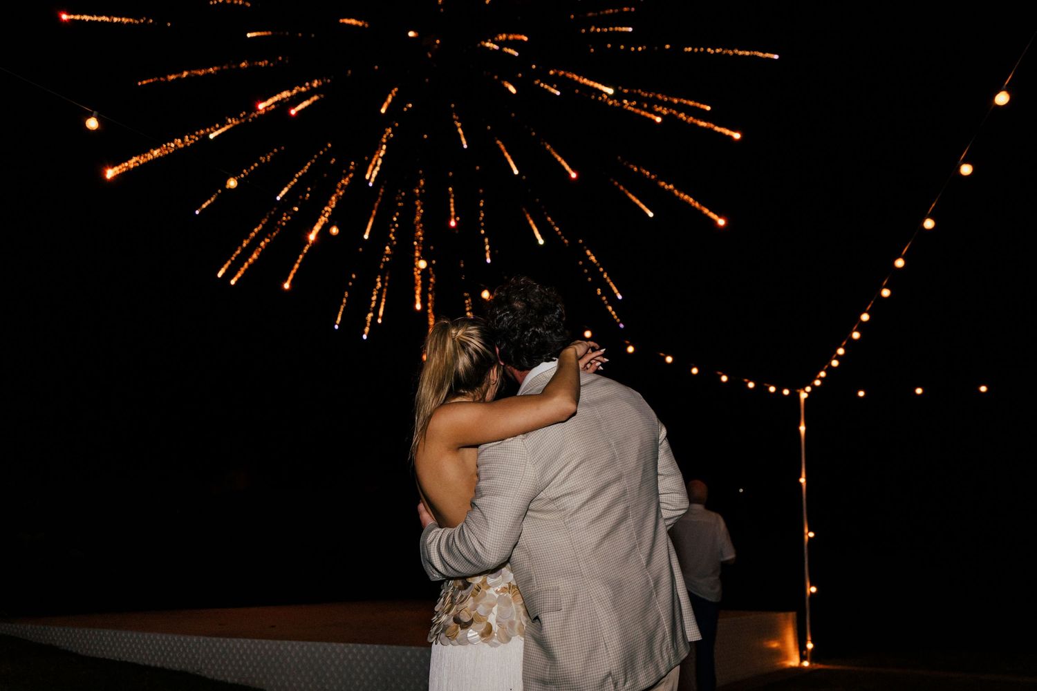 Fireworks burst in golden sparkles against the dark night sky during an outdoor celebration.