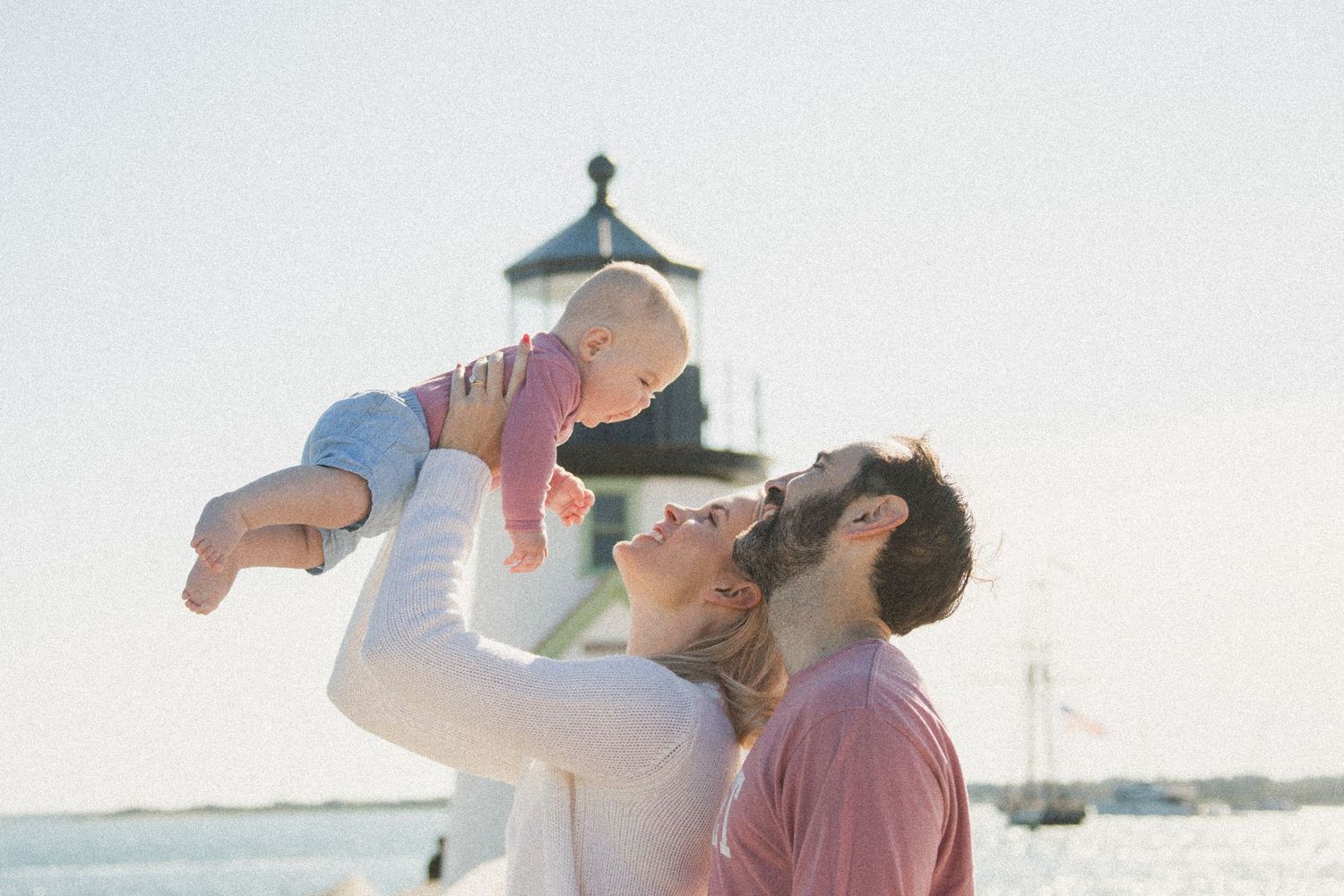 A joyful moment shared at a lighthouse with boats visible in the harbor background.