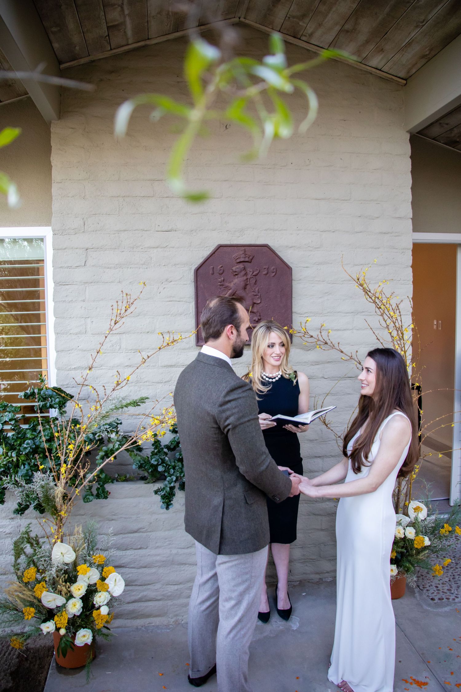 Multiple angles capture an intimate proposal moment against a white brick wall with yellow flowers.