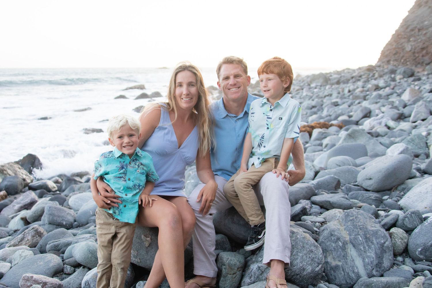 Family members relaxing on rocky beach with ocean waves in background.