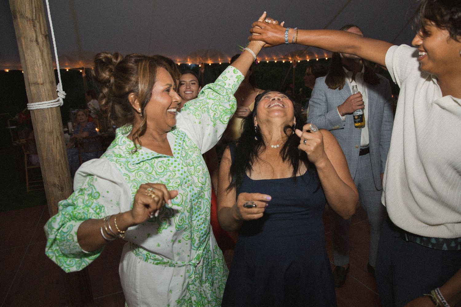 Wedding reception dance party with guests celebrating under string lights at dusk.