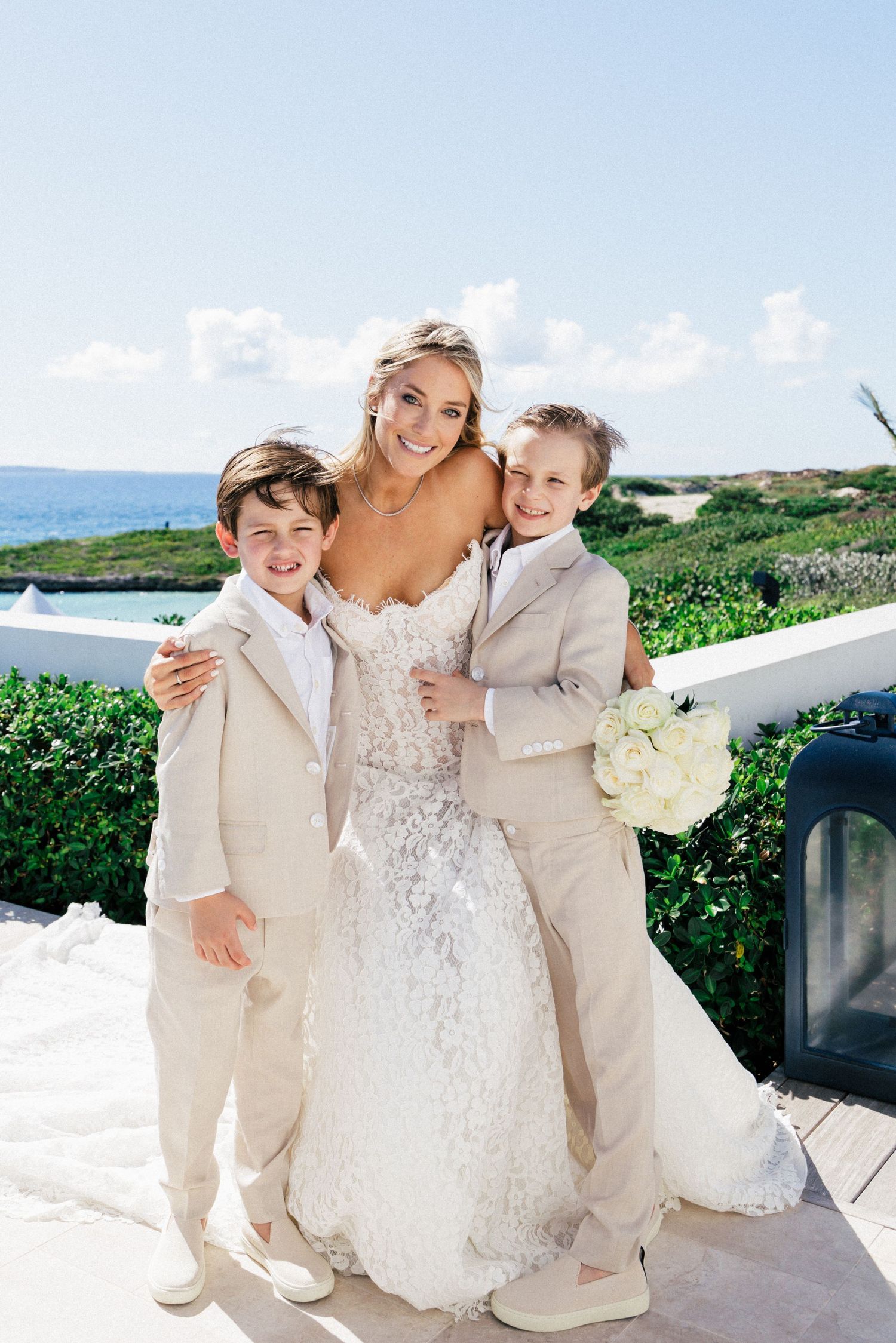 Wedding party poses on a sunny terrace with ocean views and tropical greenery.