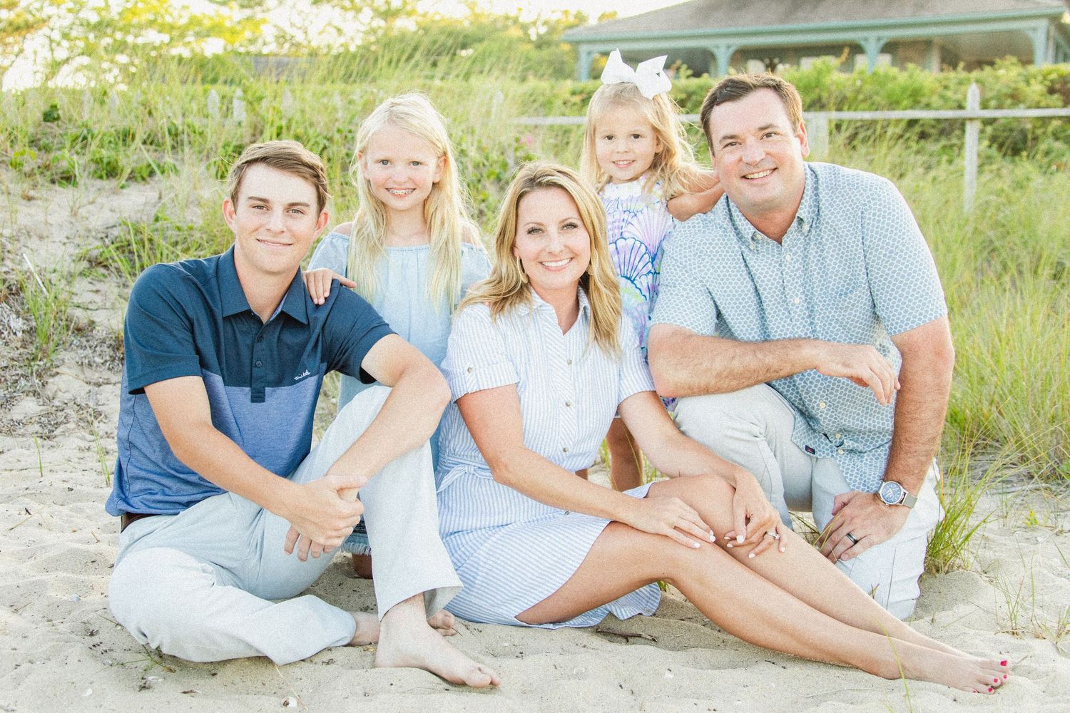 Family portrait session on a sandy beach with coordinated blue and white outfits.