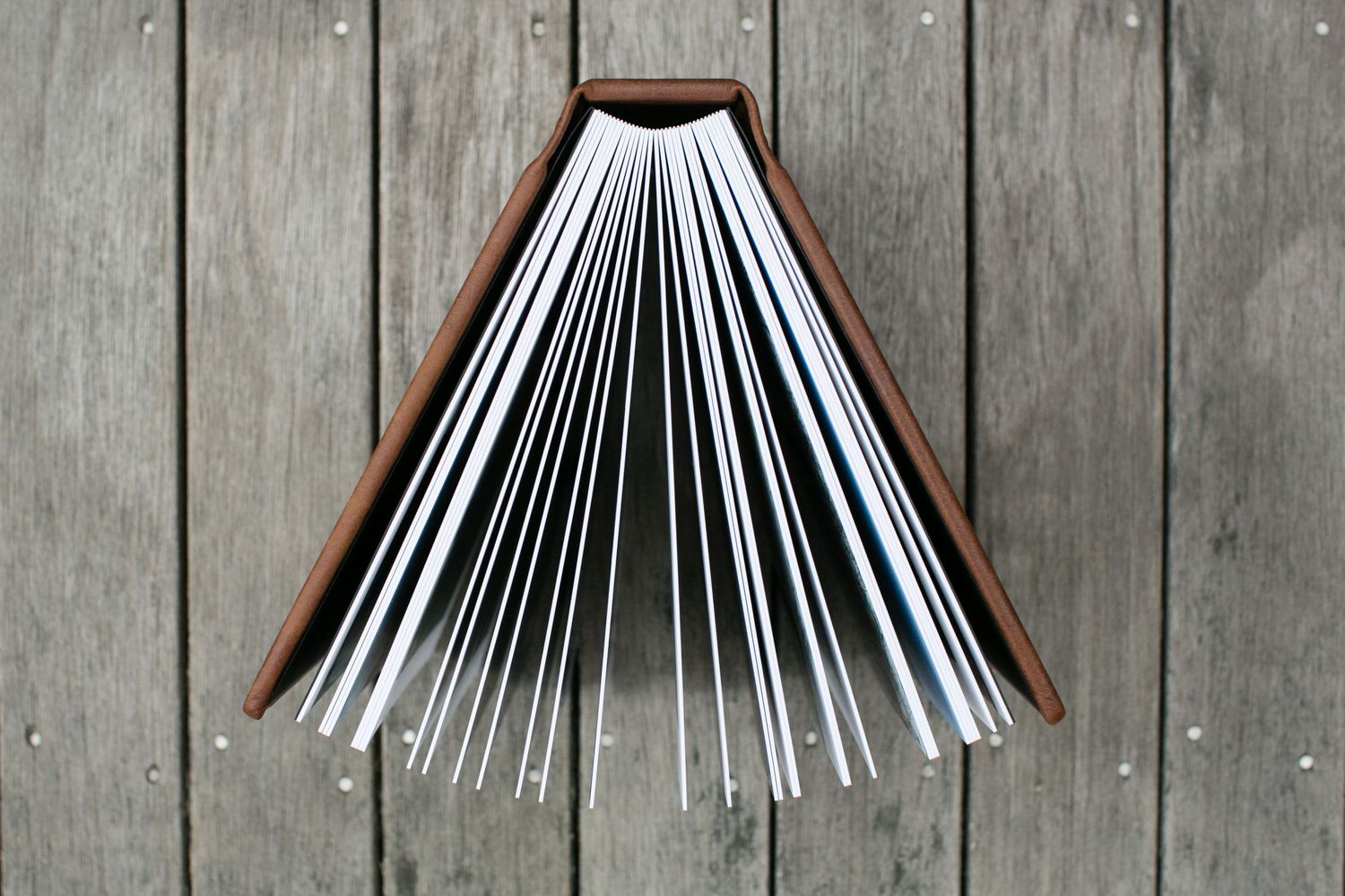 Open hardcover book fanned out against weathered wooden background showing white pages.