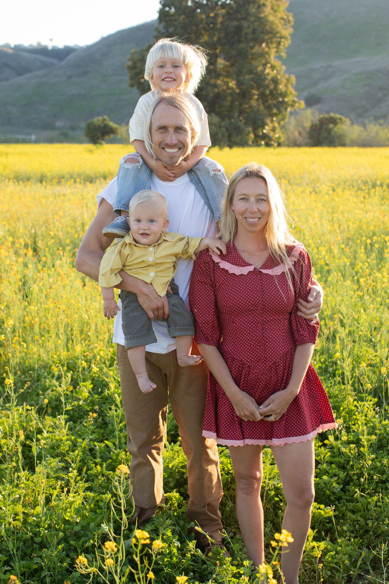 A family poses together in a vibrant yellow wildflower field with mountains in the background.