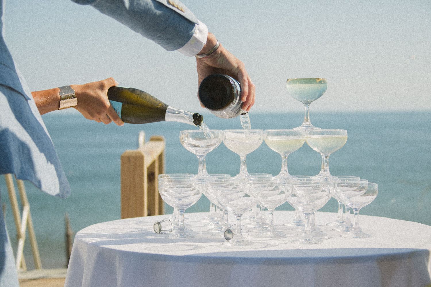 Pouring champagne into vintage coupe glass tower at oceanside celebration.