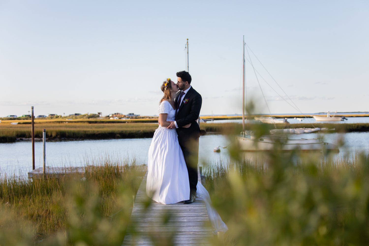 A romantic moment captured on a dock surrounded by coastal wetlands and sailboats.