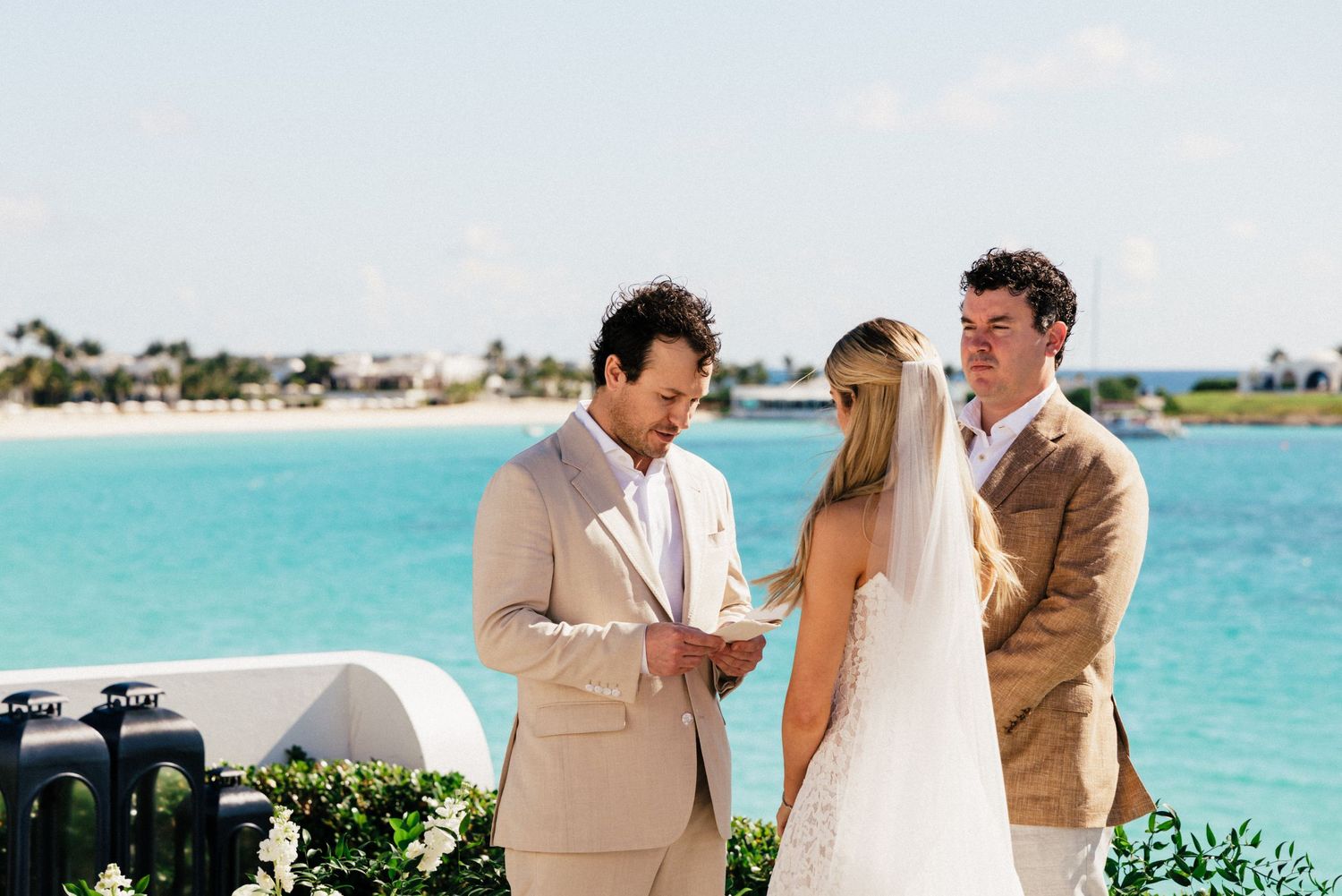 Candid moments between wedding party members on a sunny beach with turquoise waters in the background.