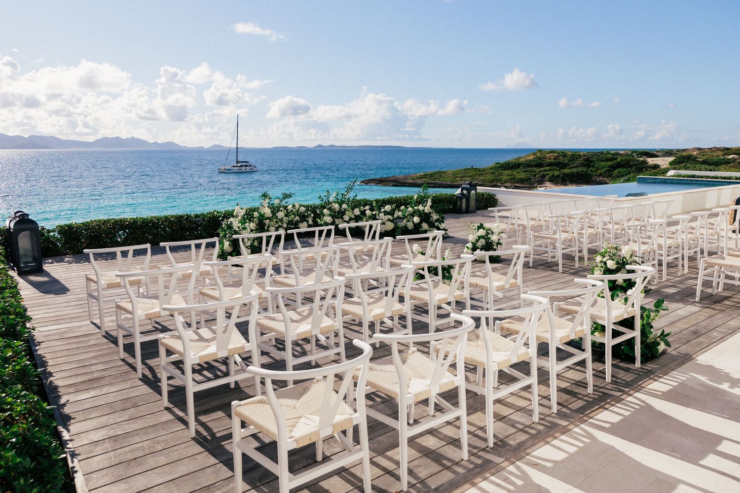 White wedding chairs arranged on oceanfront deck with tropical views.