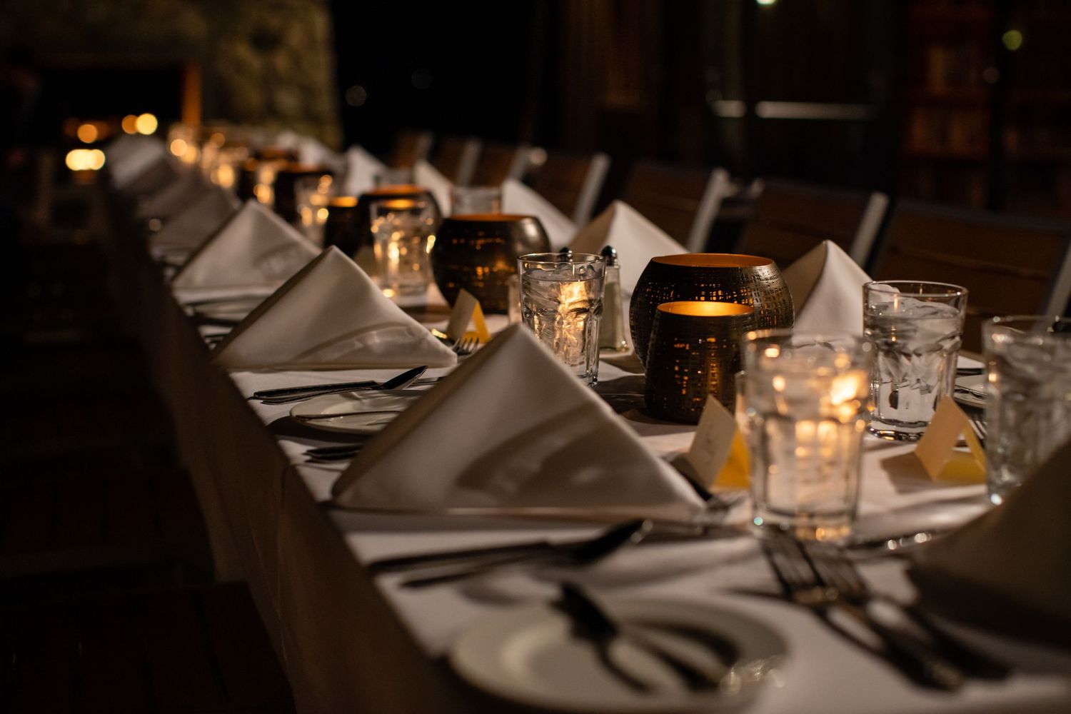 An elegant dinner table setting with white linens and glowing candles in a dimly lit room.