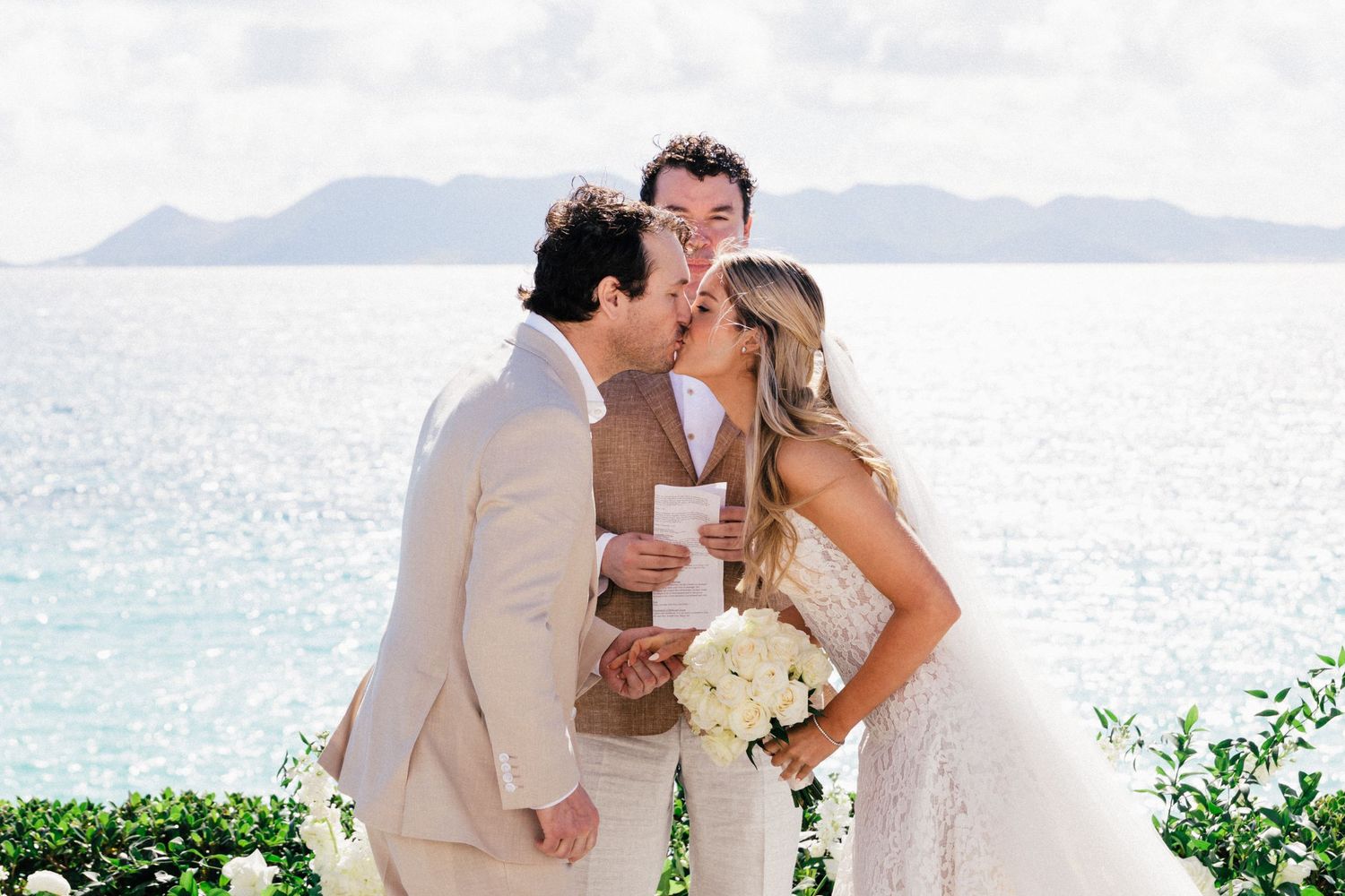 Romantic moment captured against backdrop of turquoise ocean and distant mountains.