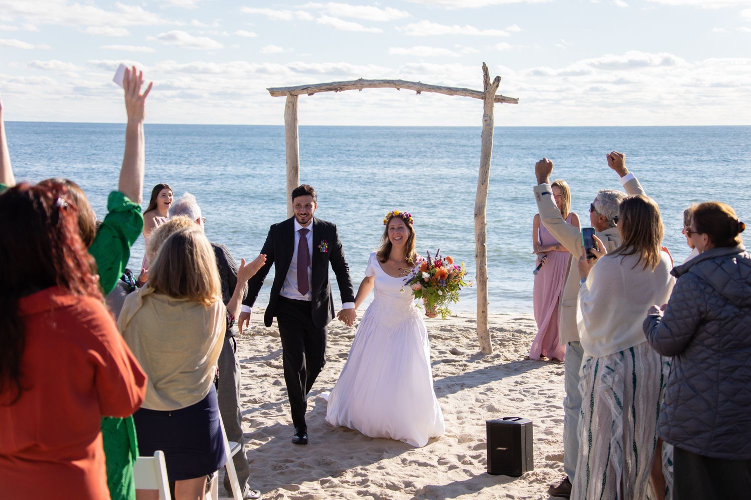 Rustic beach wedding ceremony setup with driftwood arch and guests gathered on the sand.