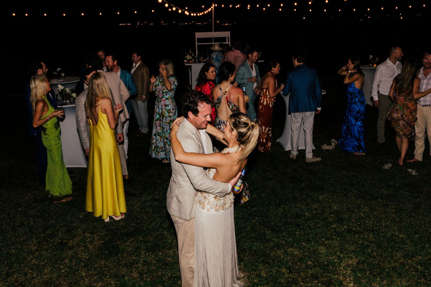 Couples dancing on a grassy outdoor dance floor under twinkling string lights.