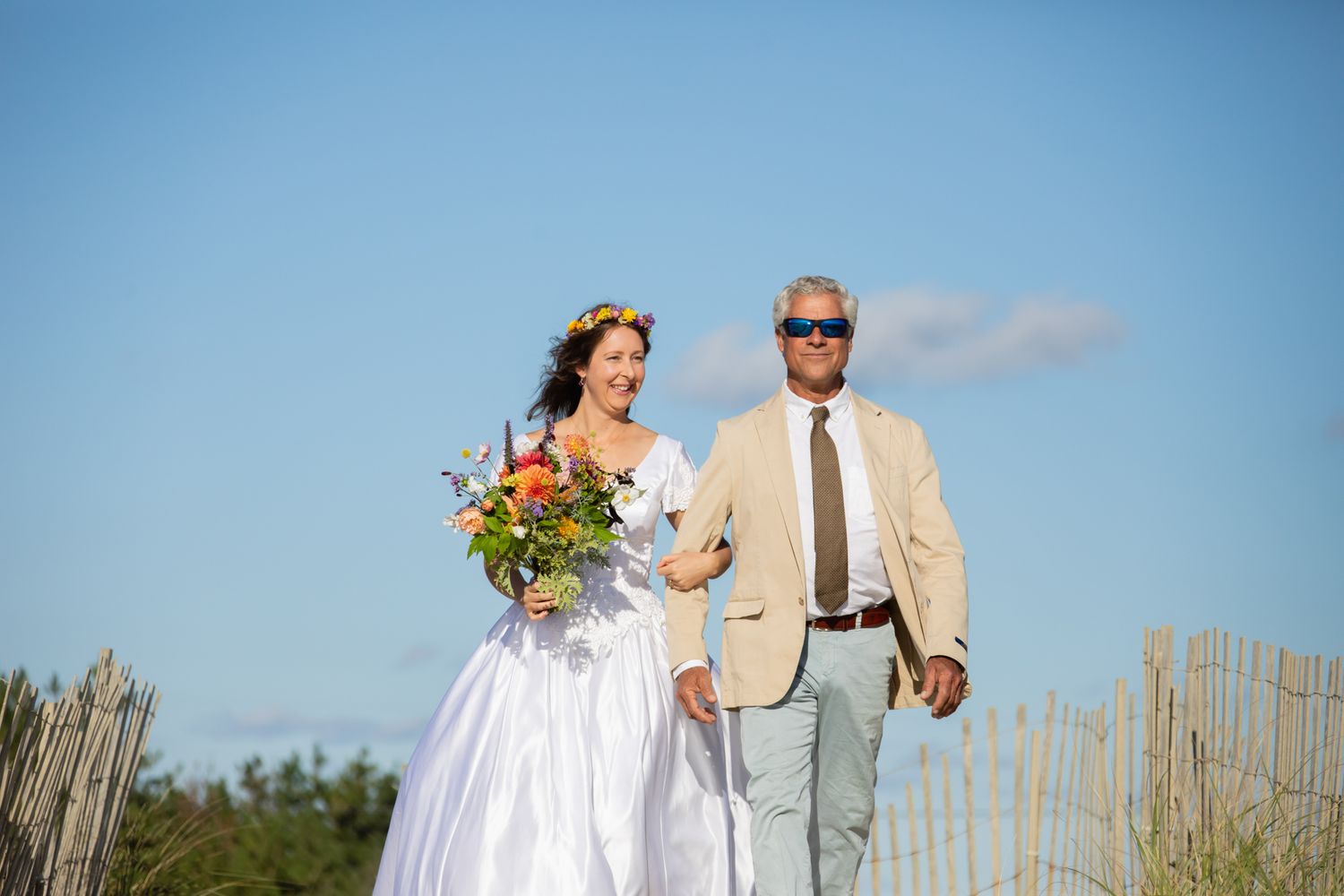 Wedding couple walking through tall beach grass during sunset photo session.