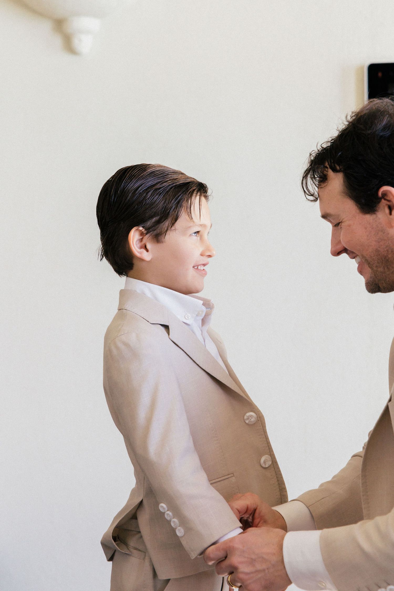 Two people in light colored suits sharing a playful moment indoors.