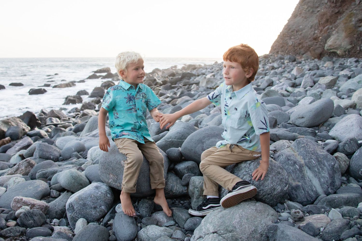 Group sitting together on dark rocks at coastal beach during sunset.