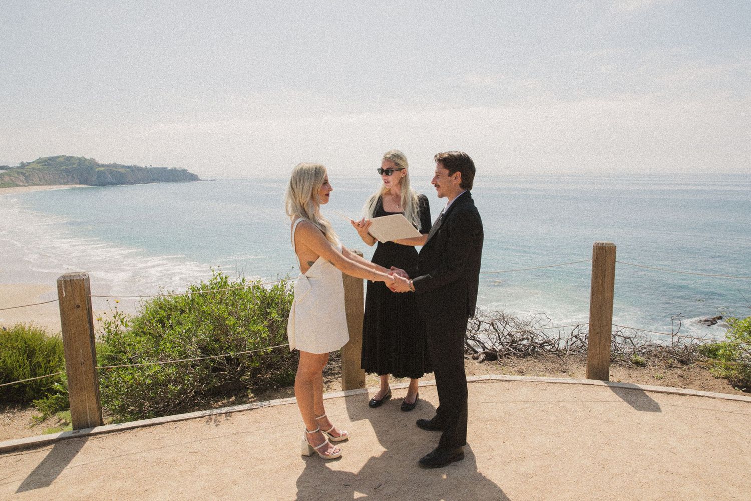 Wedding ceremony taking place on a coastal overlook with ocean views and wooden posts.