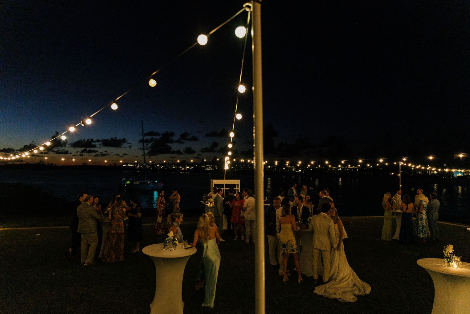 String lights illuminate an outdoor wedding reception area against a dark night sky.