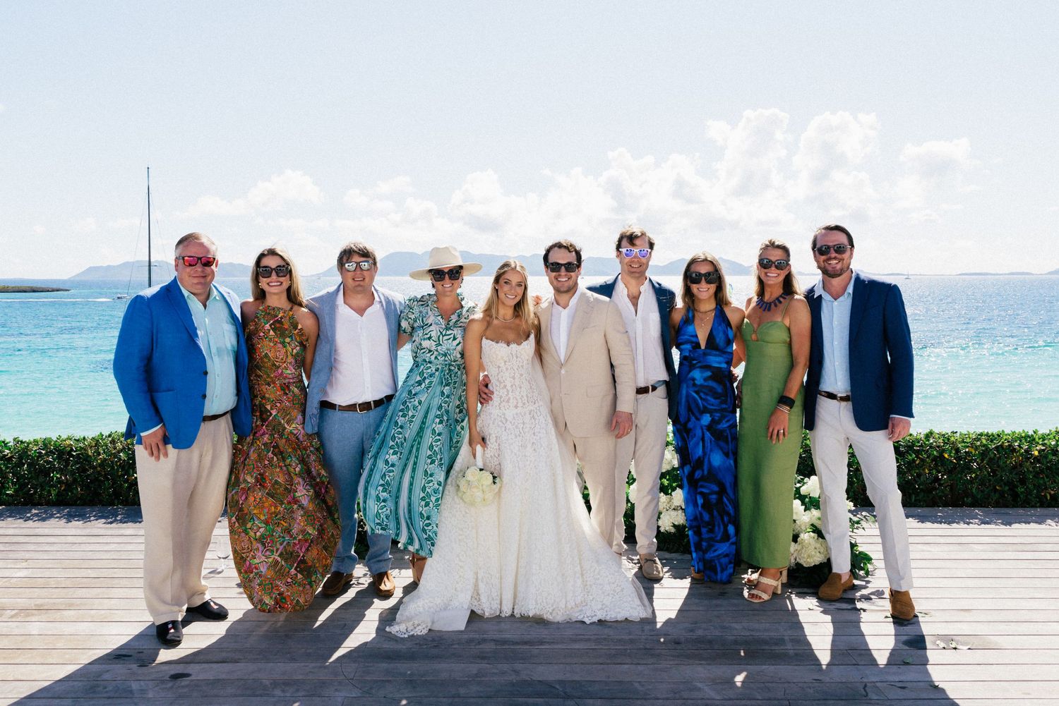 Wedding group photo on a seaside deck with guests in summer attire.