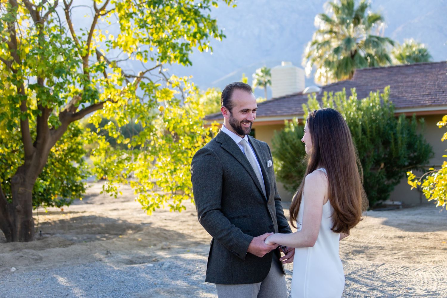 Couple holding hands in formal wear against sunny garden background.