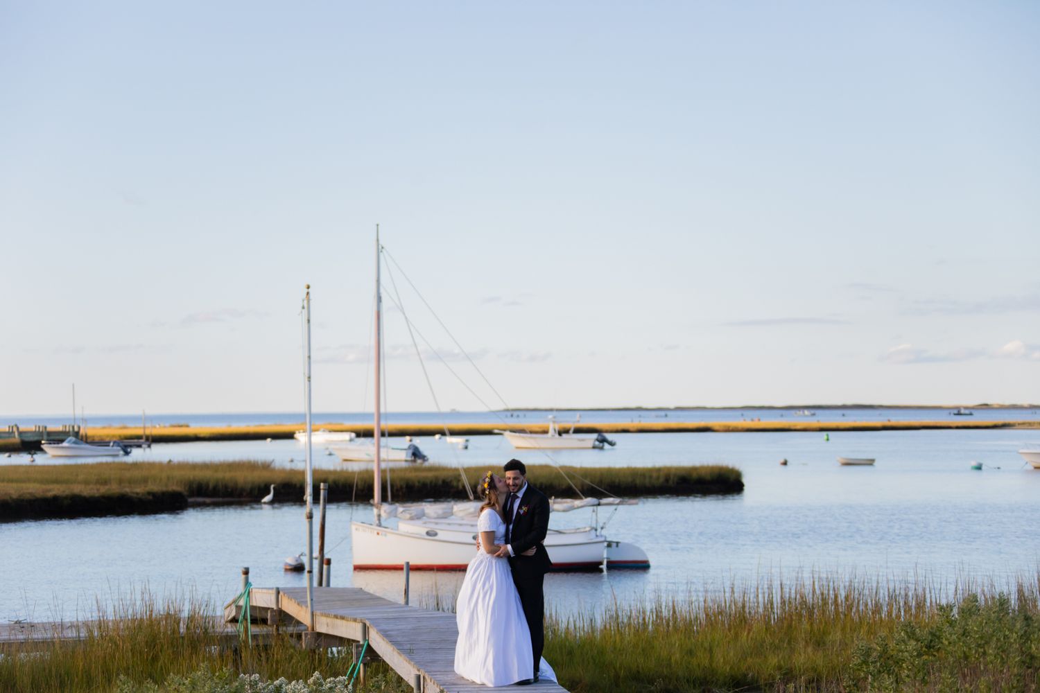 A couple embraces on a wooden dock overlooking a scenic coastal marsh at sunset.