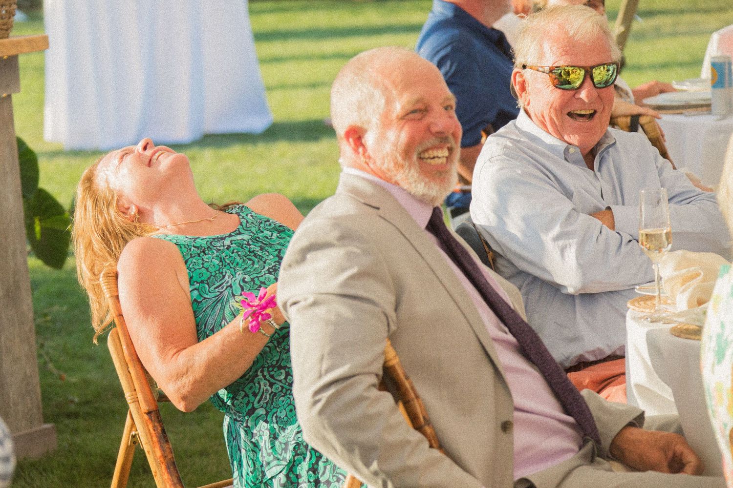 Wedding guests laugh and smile during an outdoor reception under a white tent.