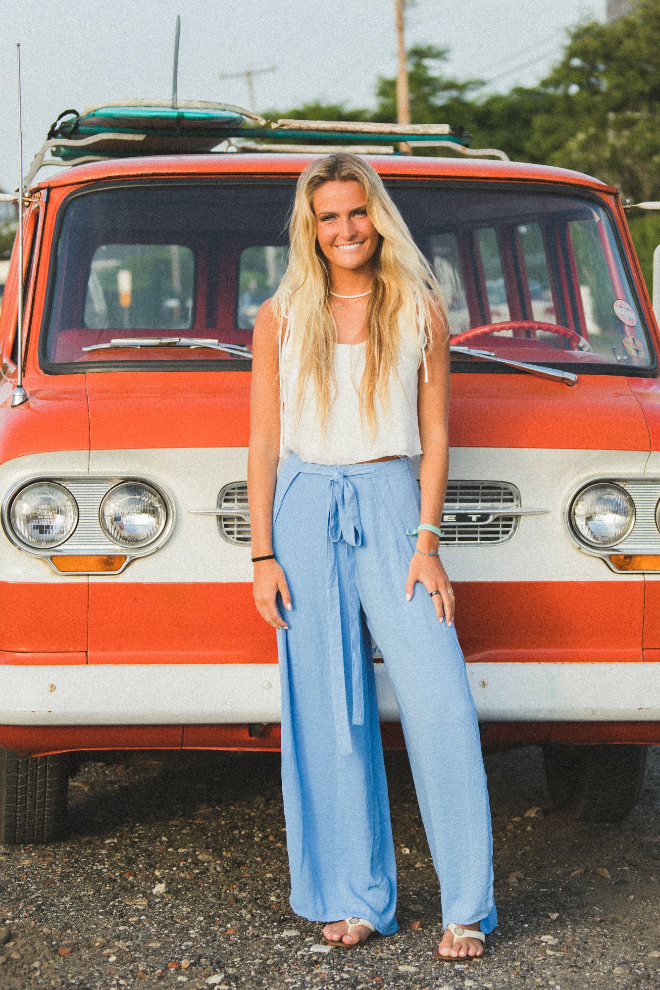 Casual fashion photo shoot featuring light blue jeans against a vintage orange and white car.