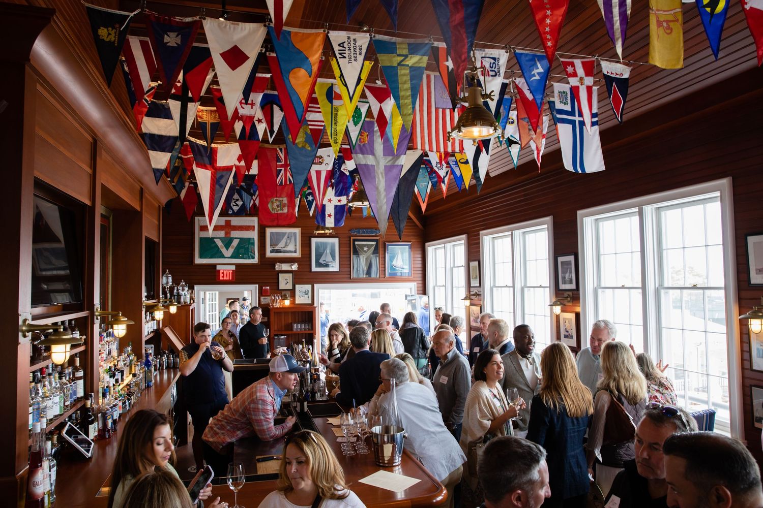 Lively nautical-themed bar adorned with colorful signal flags on ceiling, packed with patrons enjoying drinks and conversation.