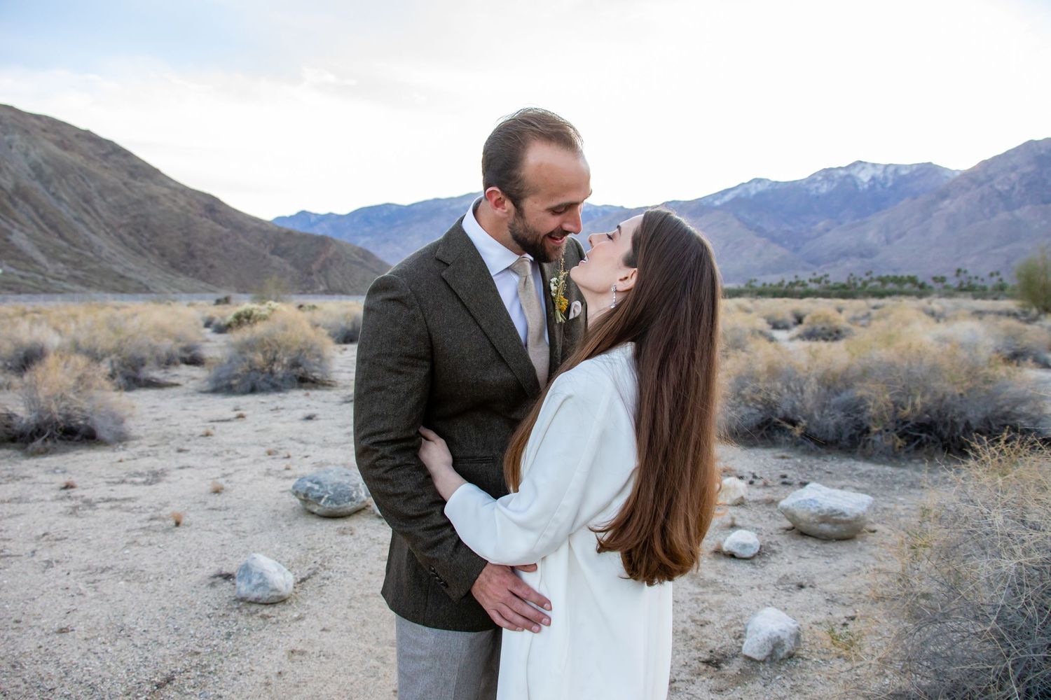 A couple shares intimate moments during their desert wedding photoshoot with mountains behind them.