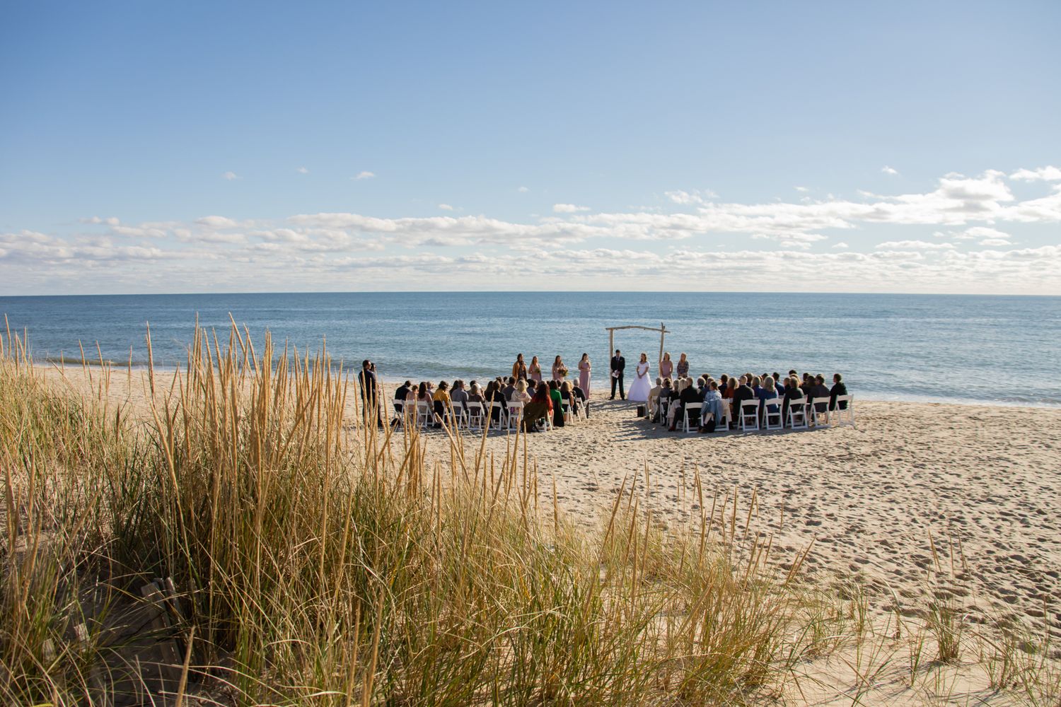 A scenic beach wedding setup with white chairs and ocean views under blue skies.