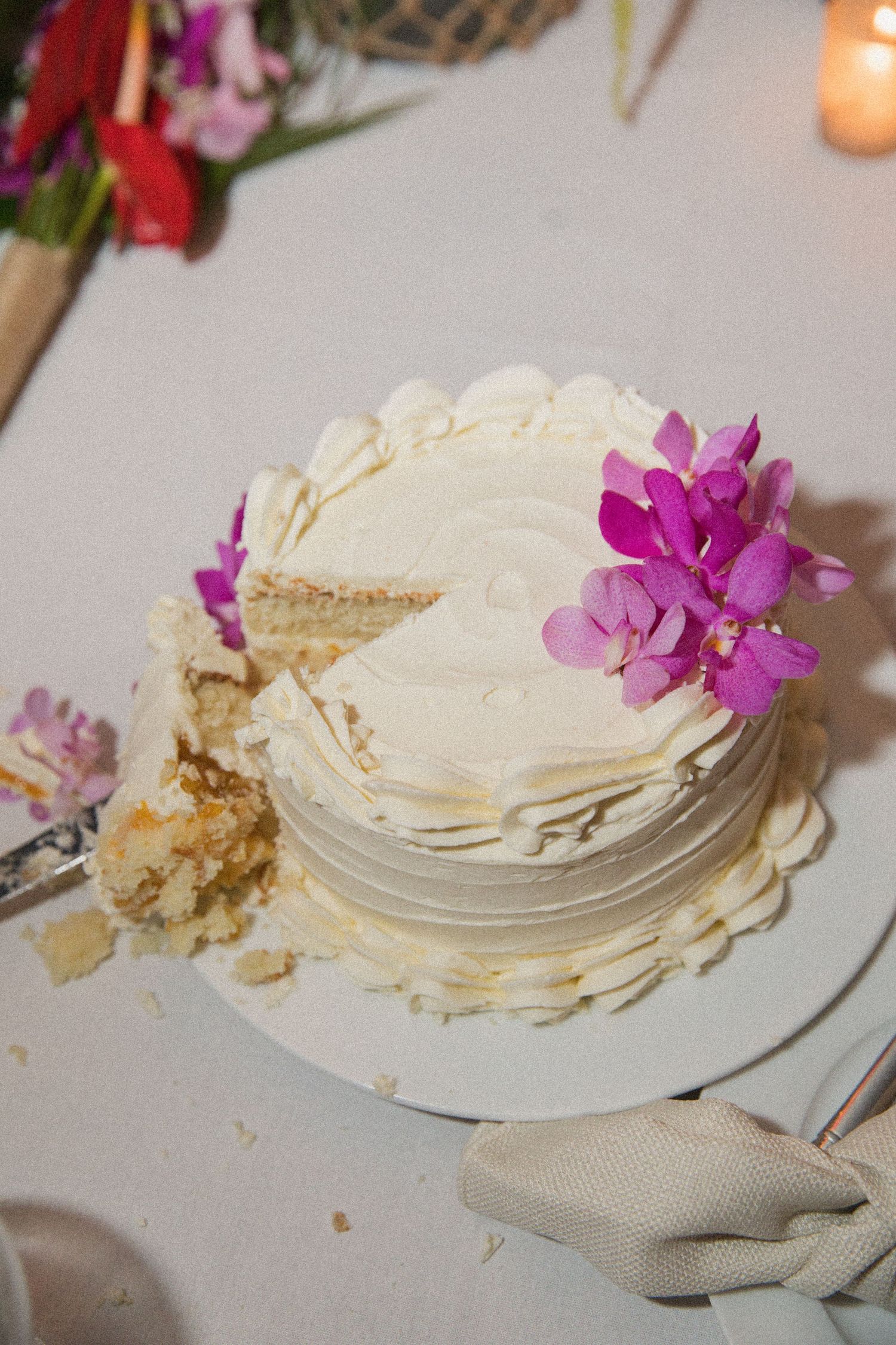 White wedding cake with purple orchid decorations and scattered crumbs on plate.