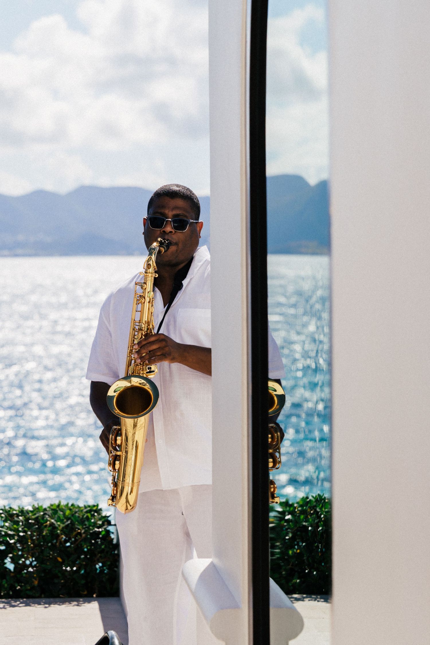 Saxophone player in white performing by window with ocean view.