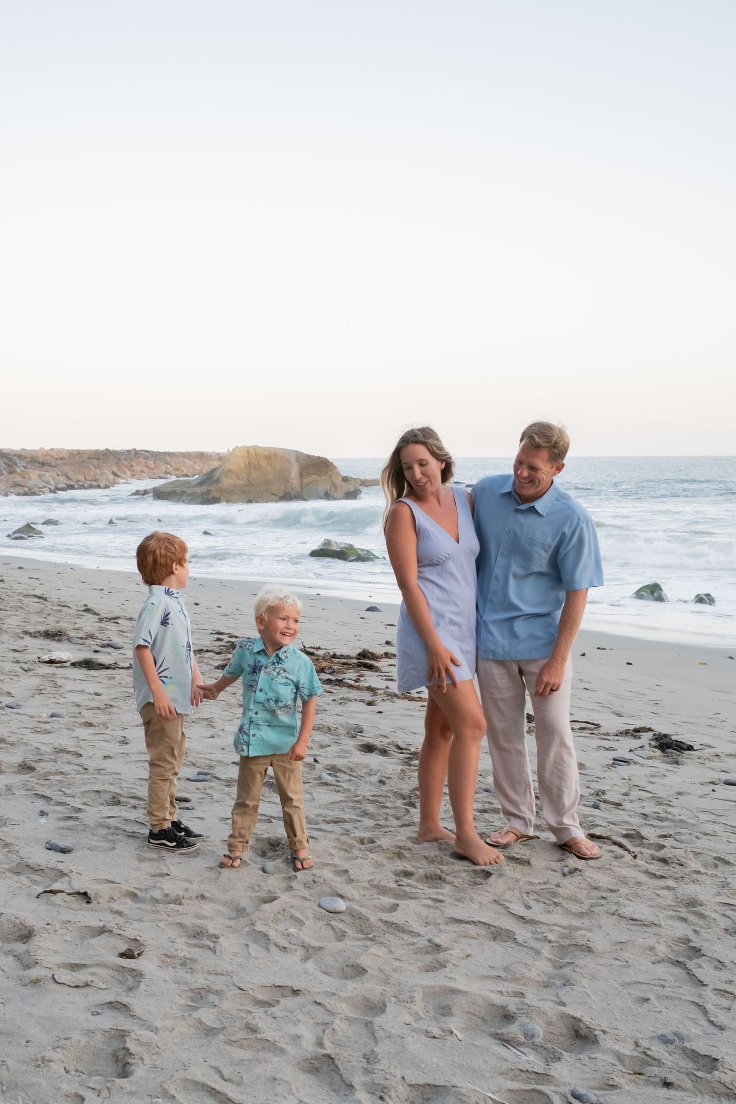 A family stands together on sandy beach with ocean and cliffs in background.