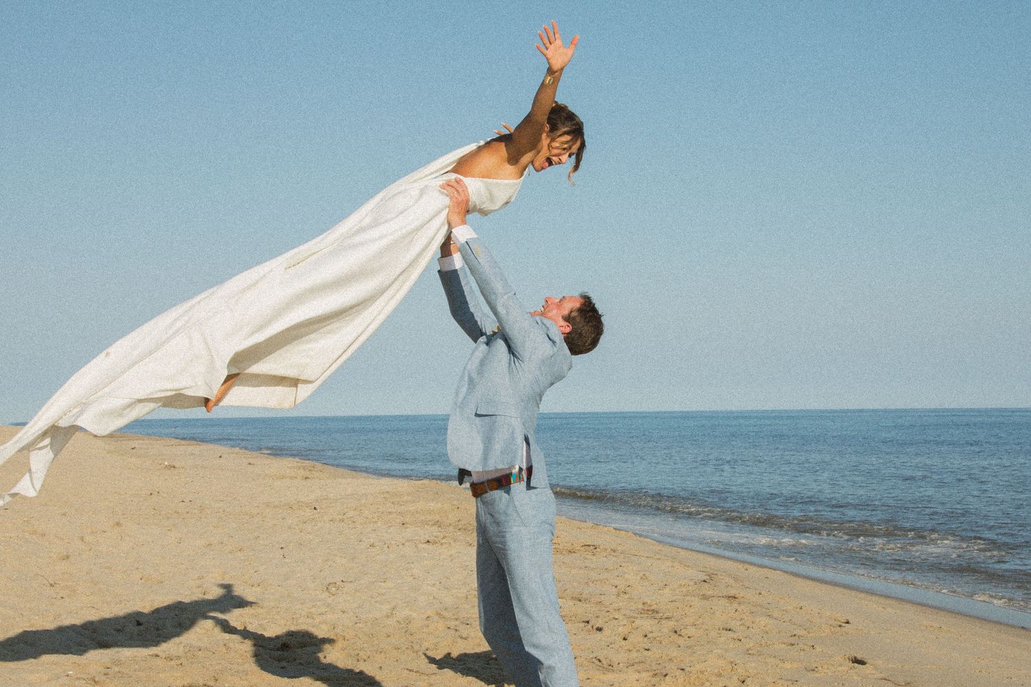Playful beach wedding moment with dramatic lift pose against ocean backdrop.
