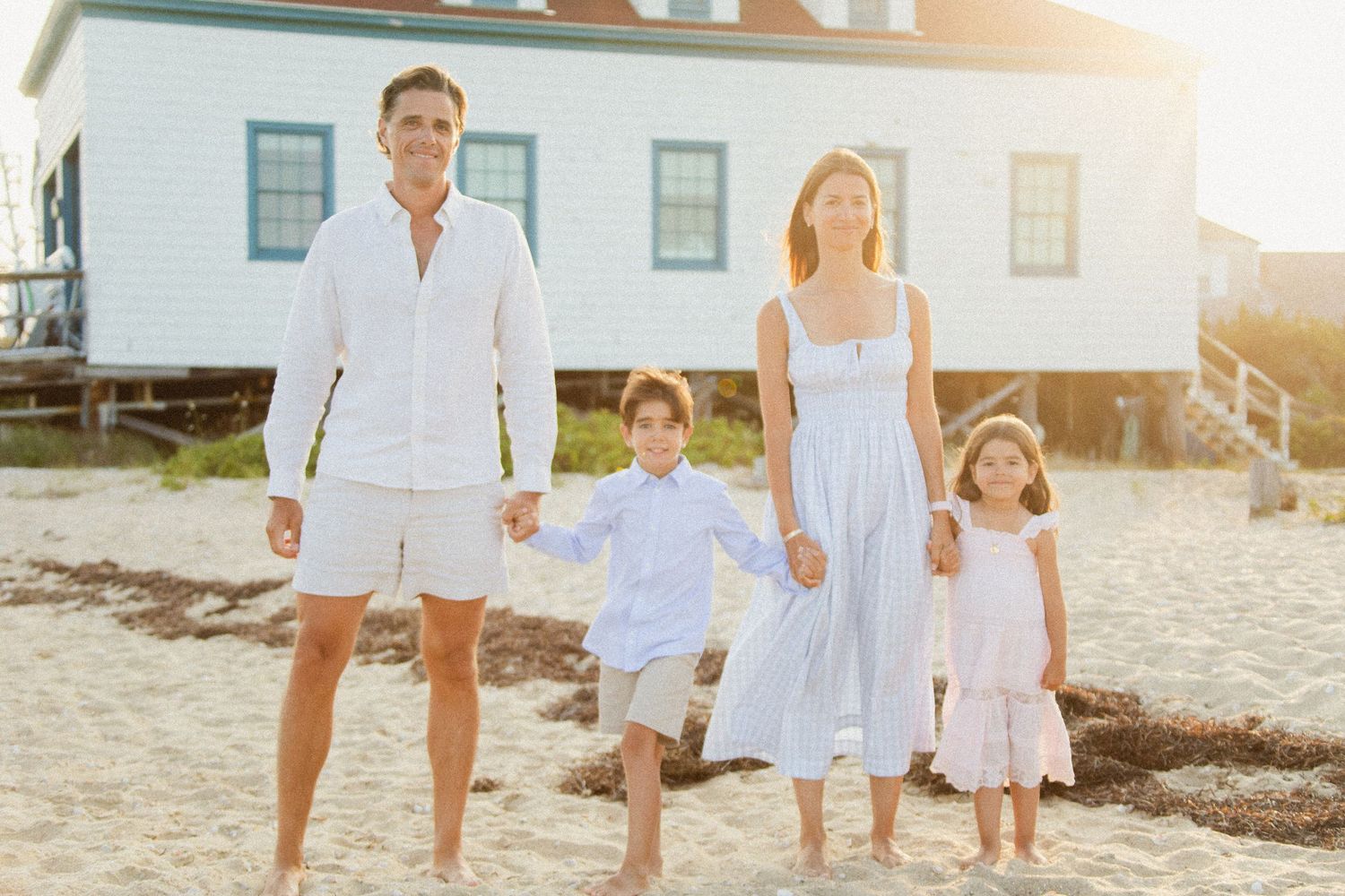 Family walking together on a beach at sunset wearing coordinated white outfits.
