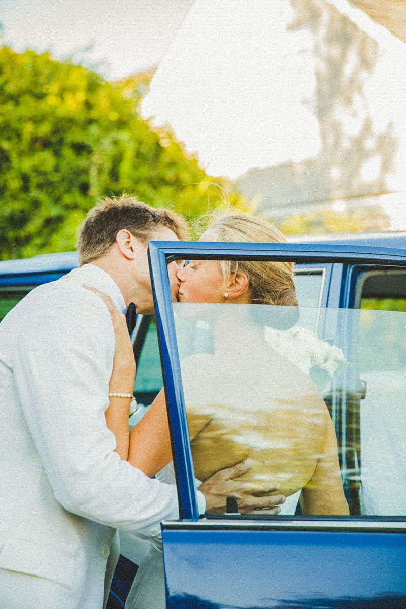Romantic couple sharing a kiss through vintage blue car window.