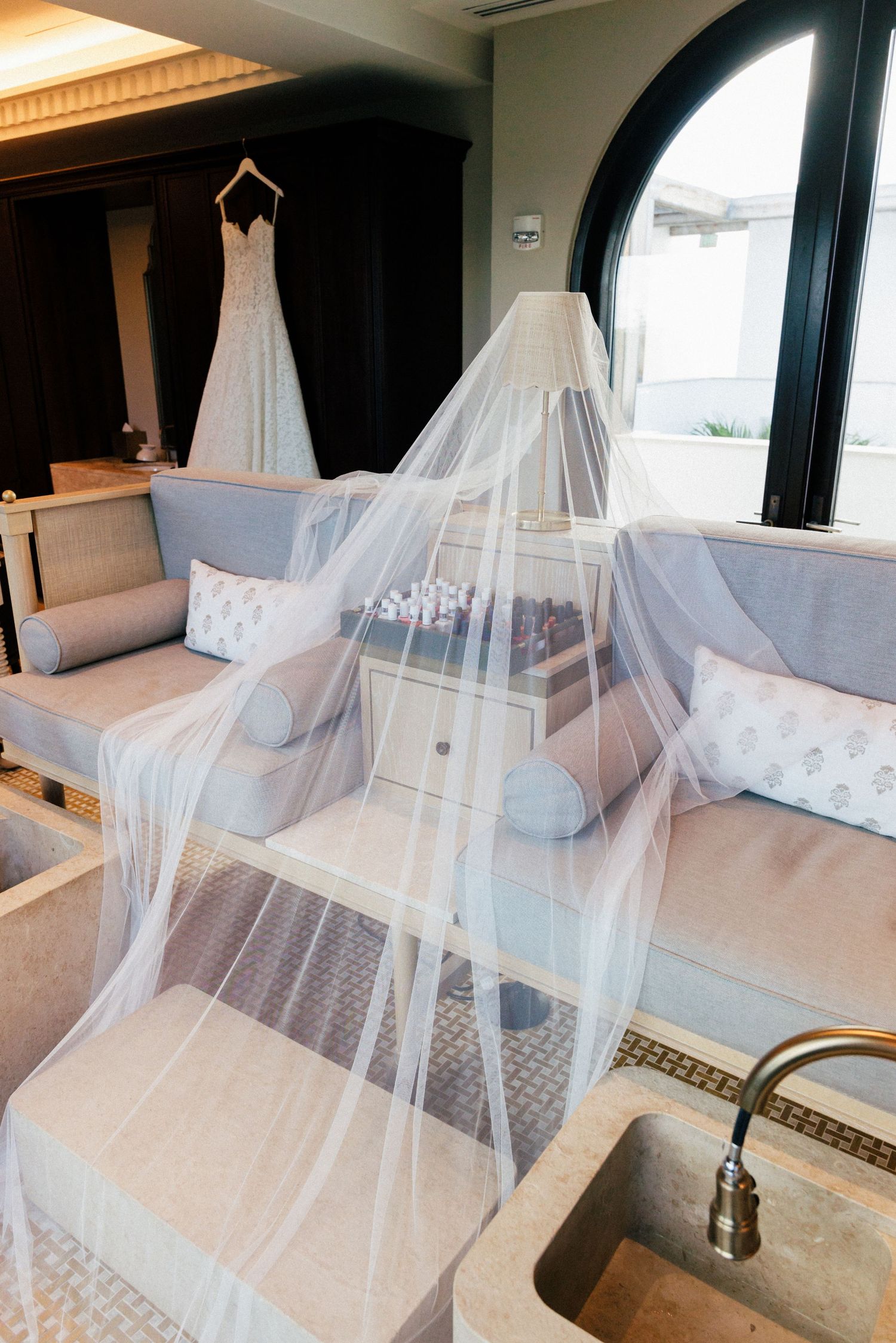Wedding dress displayed on a hanger with flowing white veil in an elegant hotel suite.