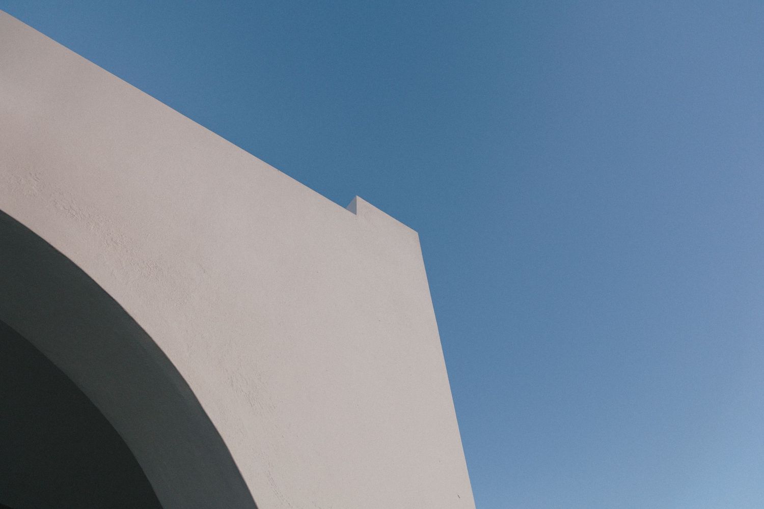 Minimalist architectural detail showing a white curved wall against bright blue sky.