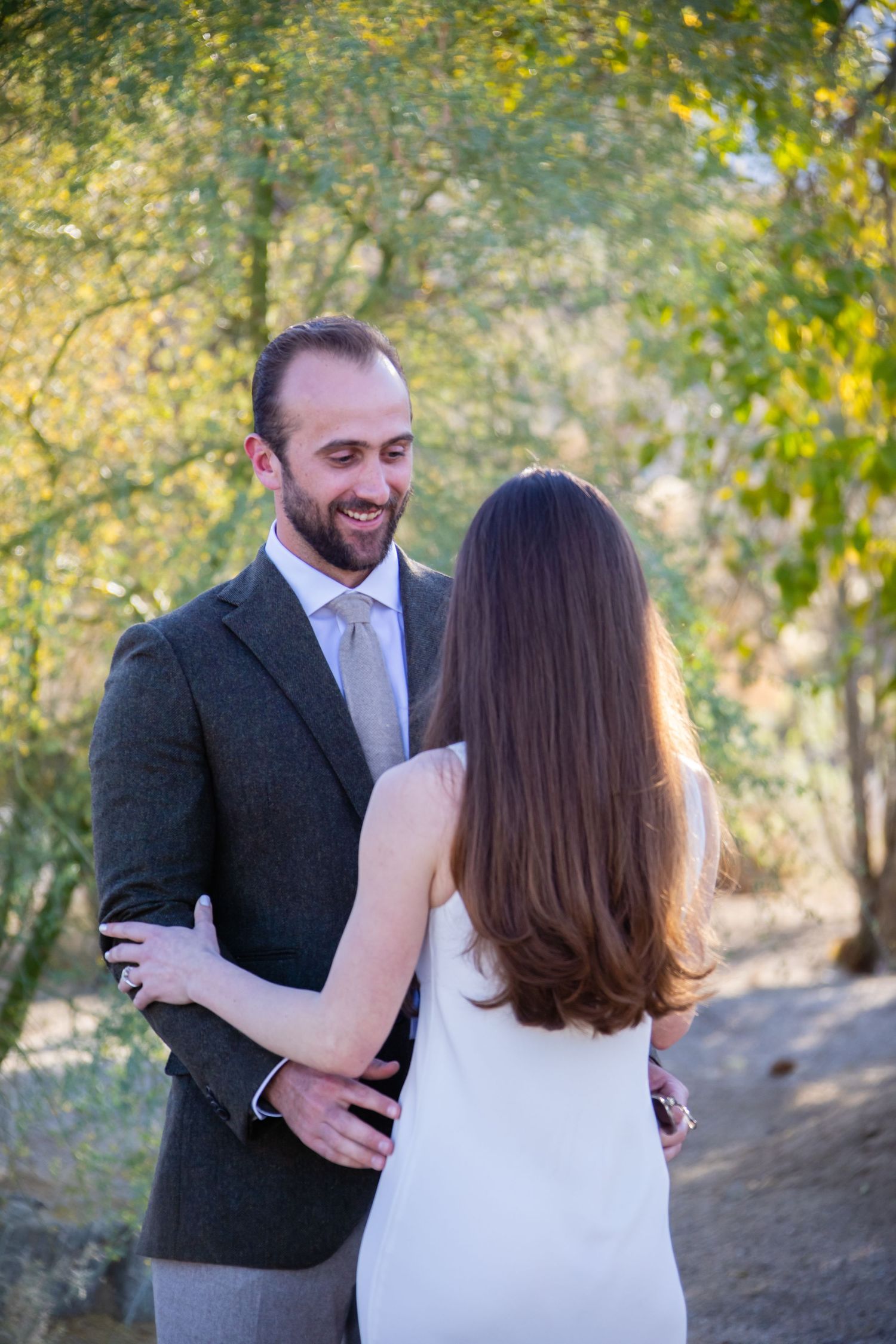 Couple in wedding attire embracing outdoors with autumn foliage.