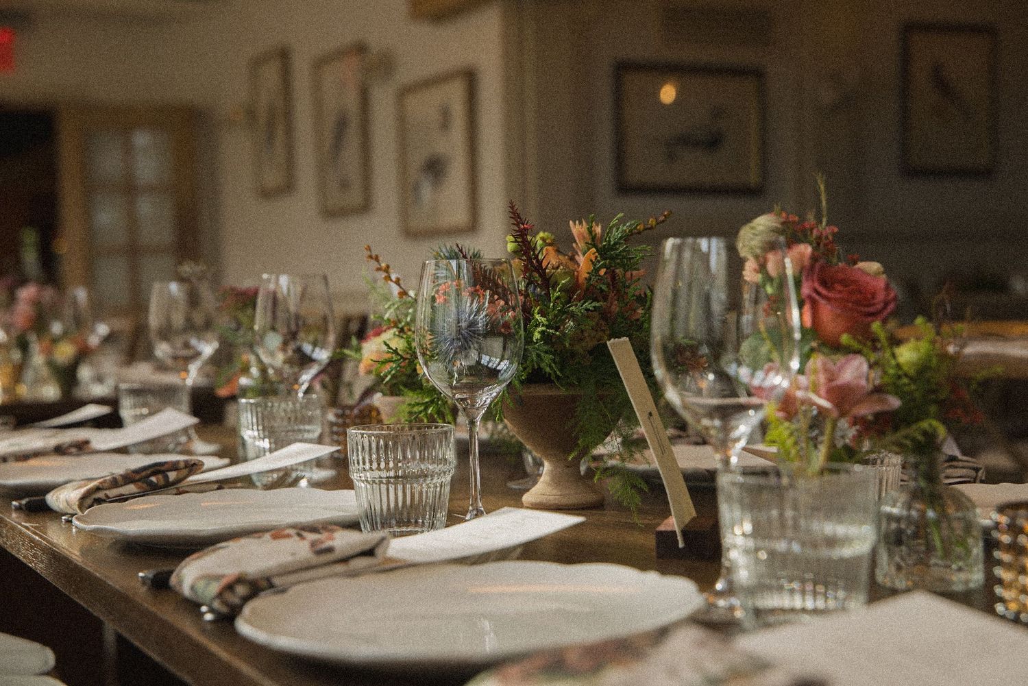 Elegant wedding reception table set with white plates, crystal glassware, and rustic floral centerpieces in warm autumn tones.