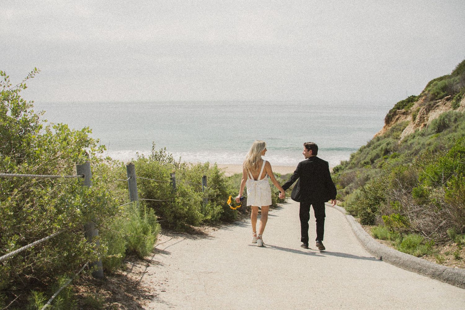 Couple walking hand in hand on scenic coastal path overlooking the ocean.