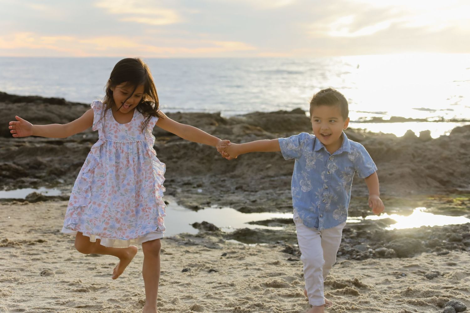 Two children play and dance together on a rocky beach during golden hour.
