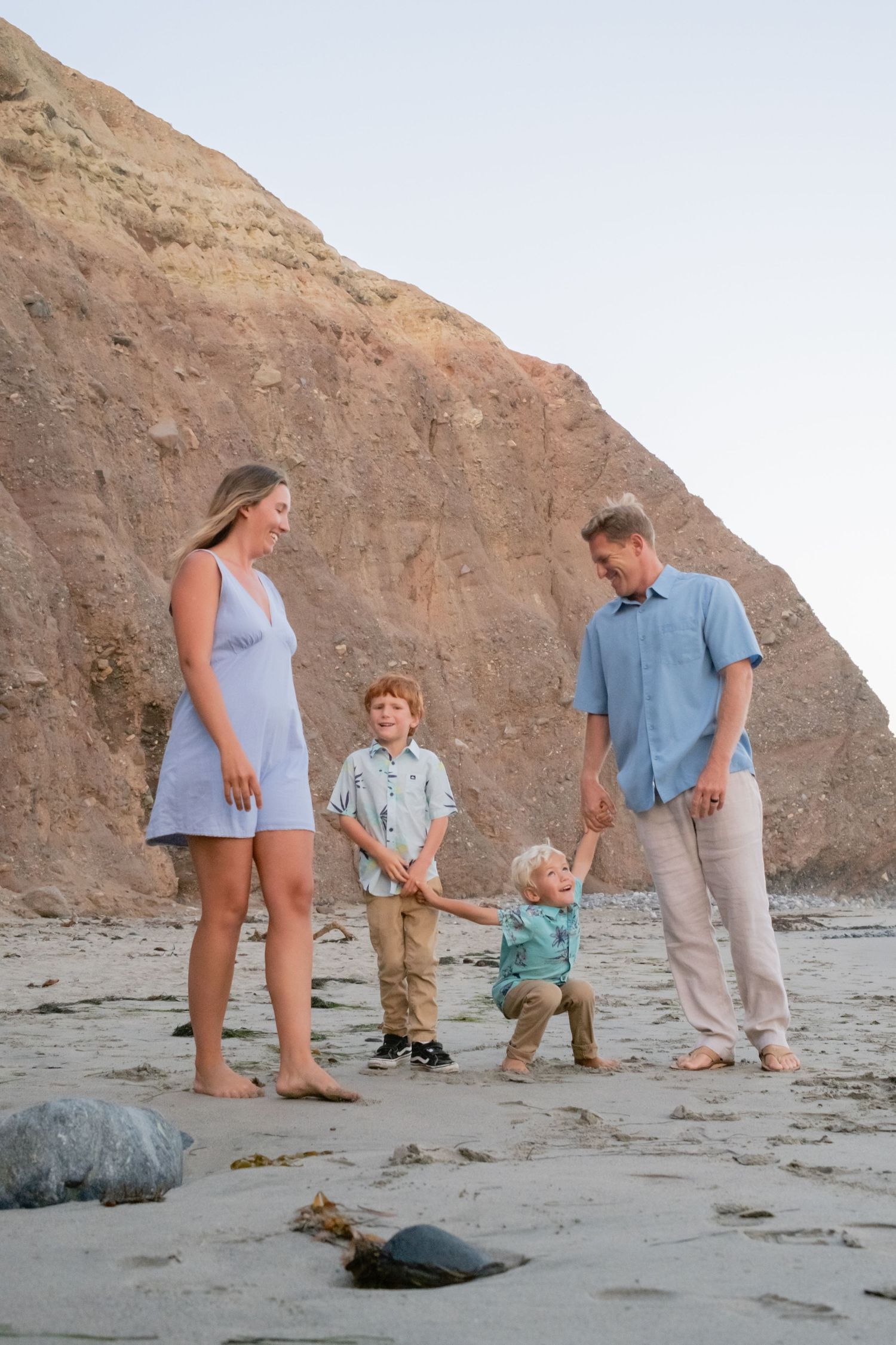 Family members standing on sandy beach near tall coastal cliffs at dusk.
