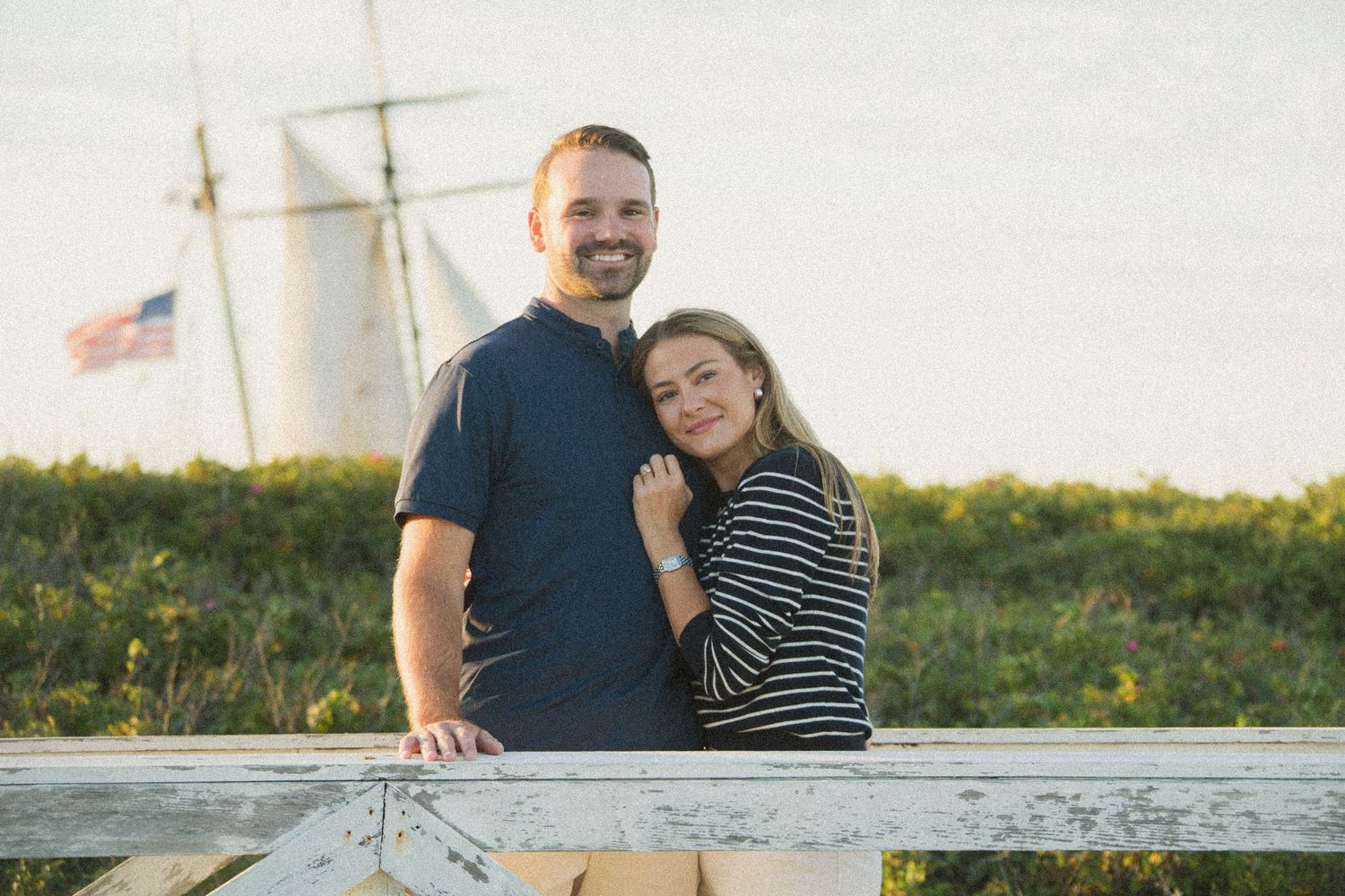 Couple enjoying a tender moment together near a lighthouse during golden hour.