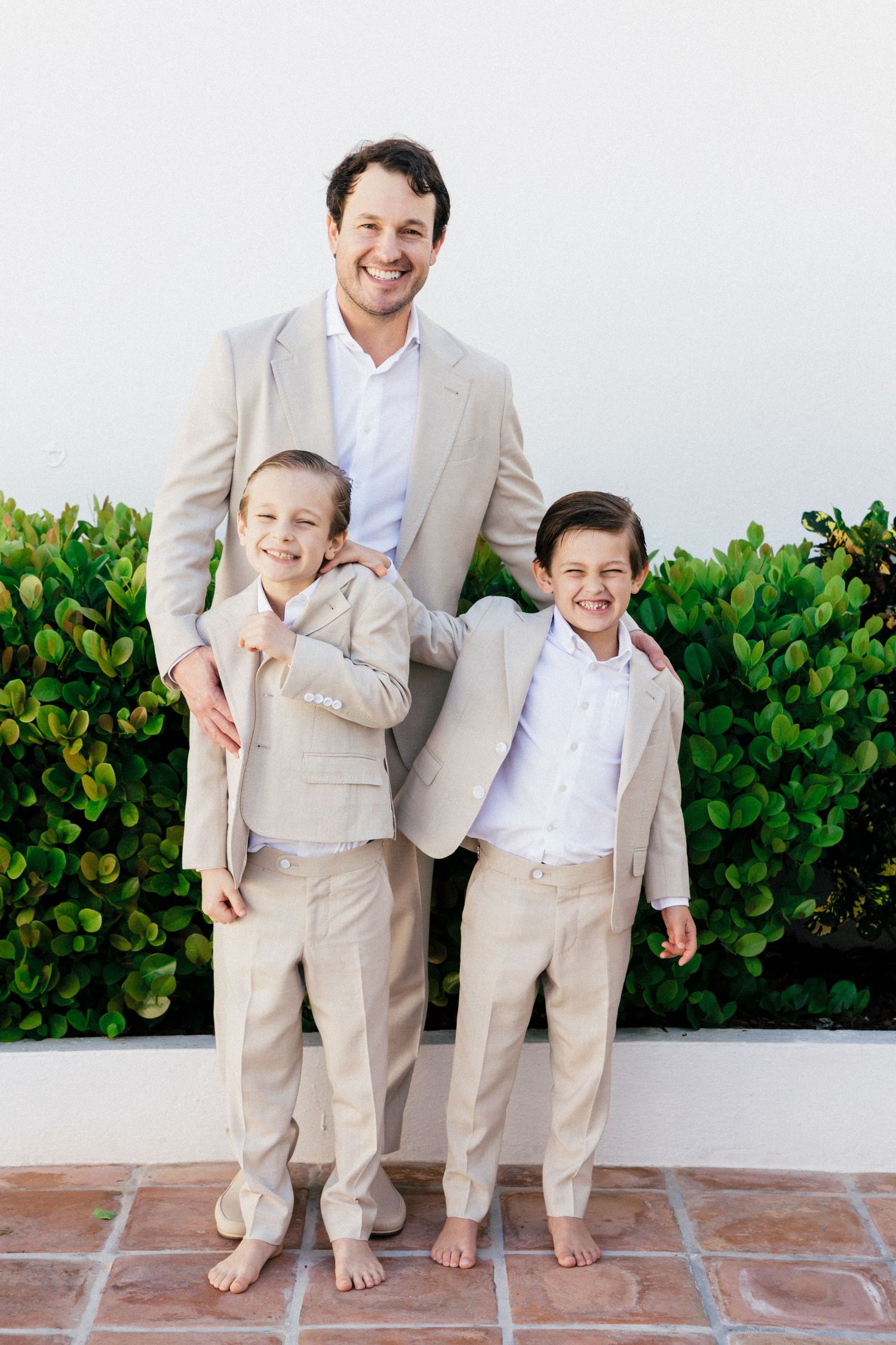 Family group in coordinated beige suits smiling and posing on terracotta tiles.