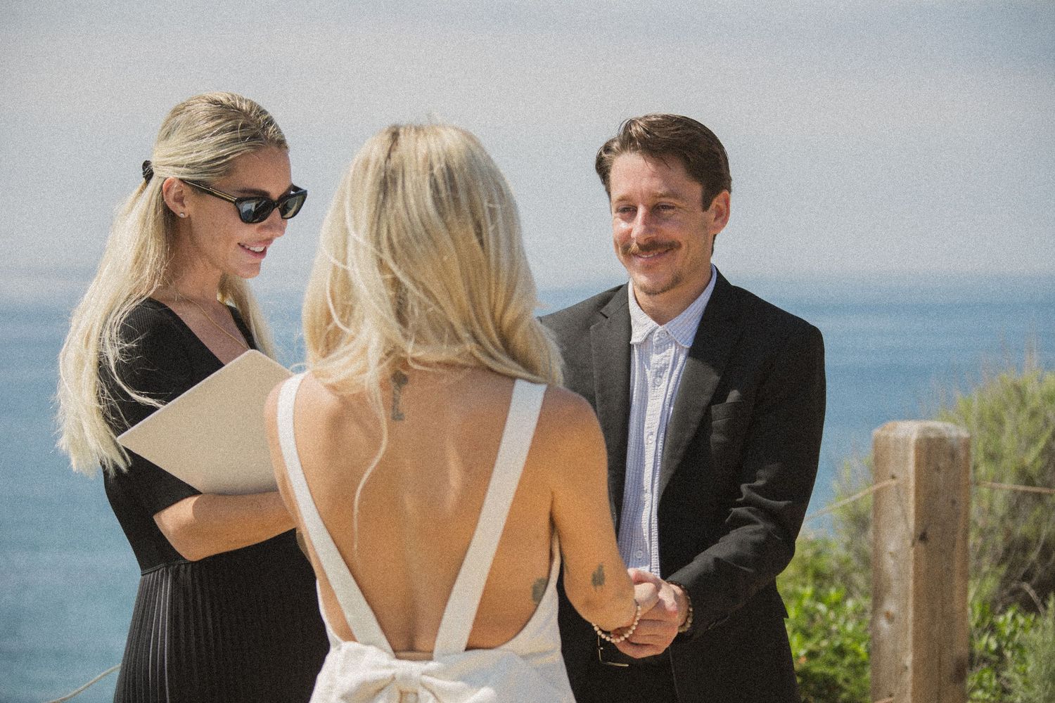 Intimate wedding ceremony with ocean backdrop and wooden fence posts.
