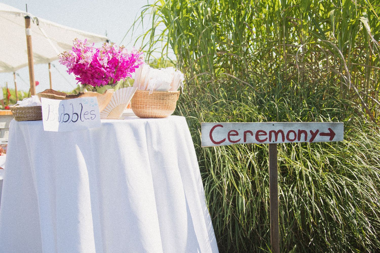 White reception tables decorated with bright pink flowers and rustic coastal elements.